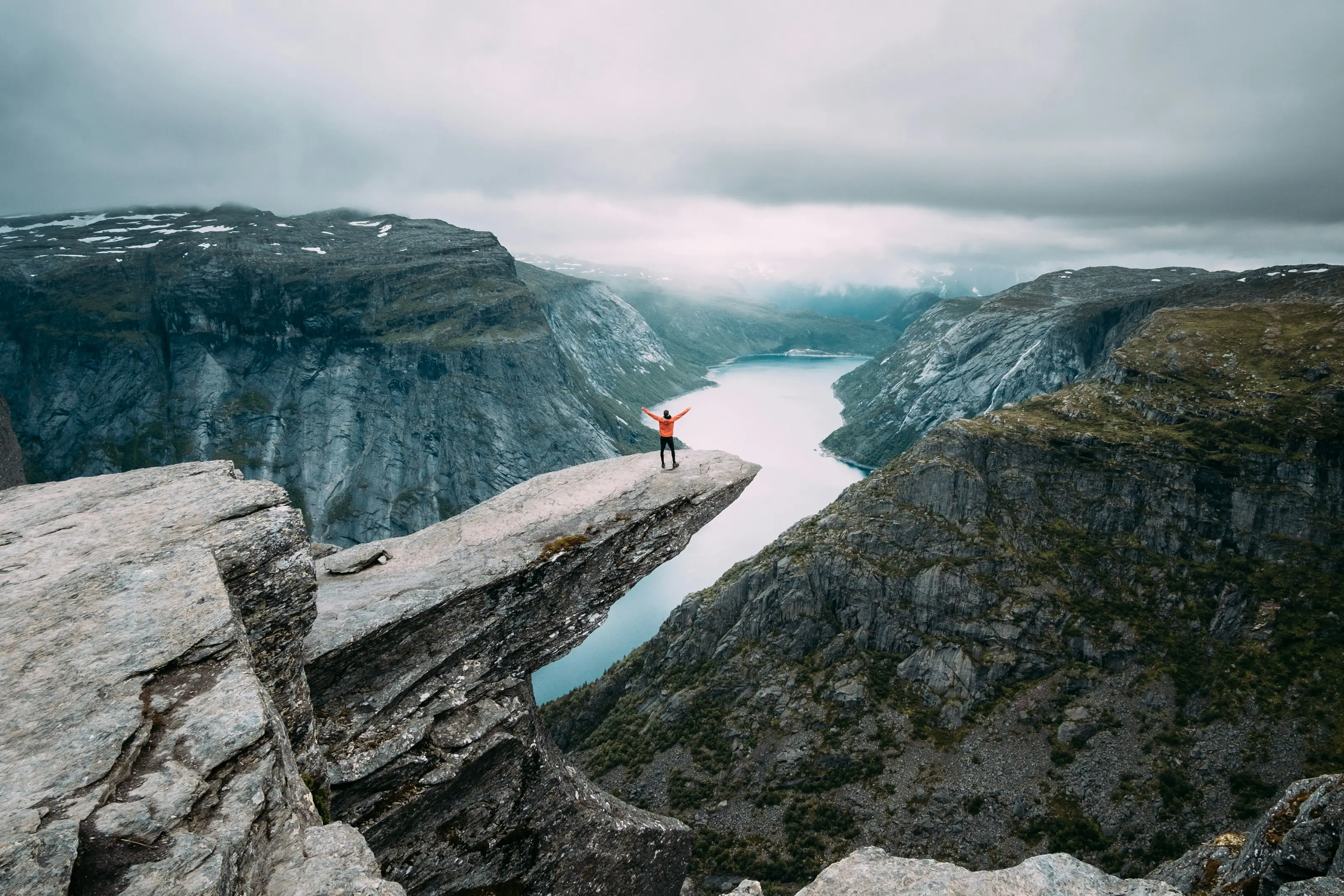 Standing on the Trolltunga ledge above a fjord in moody light