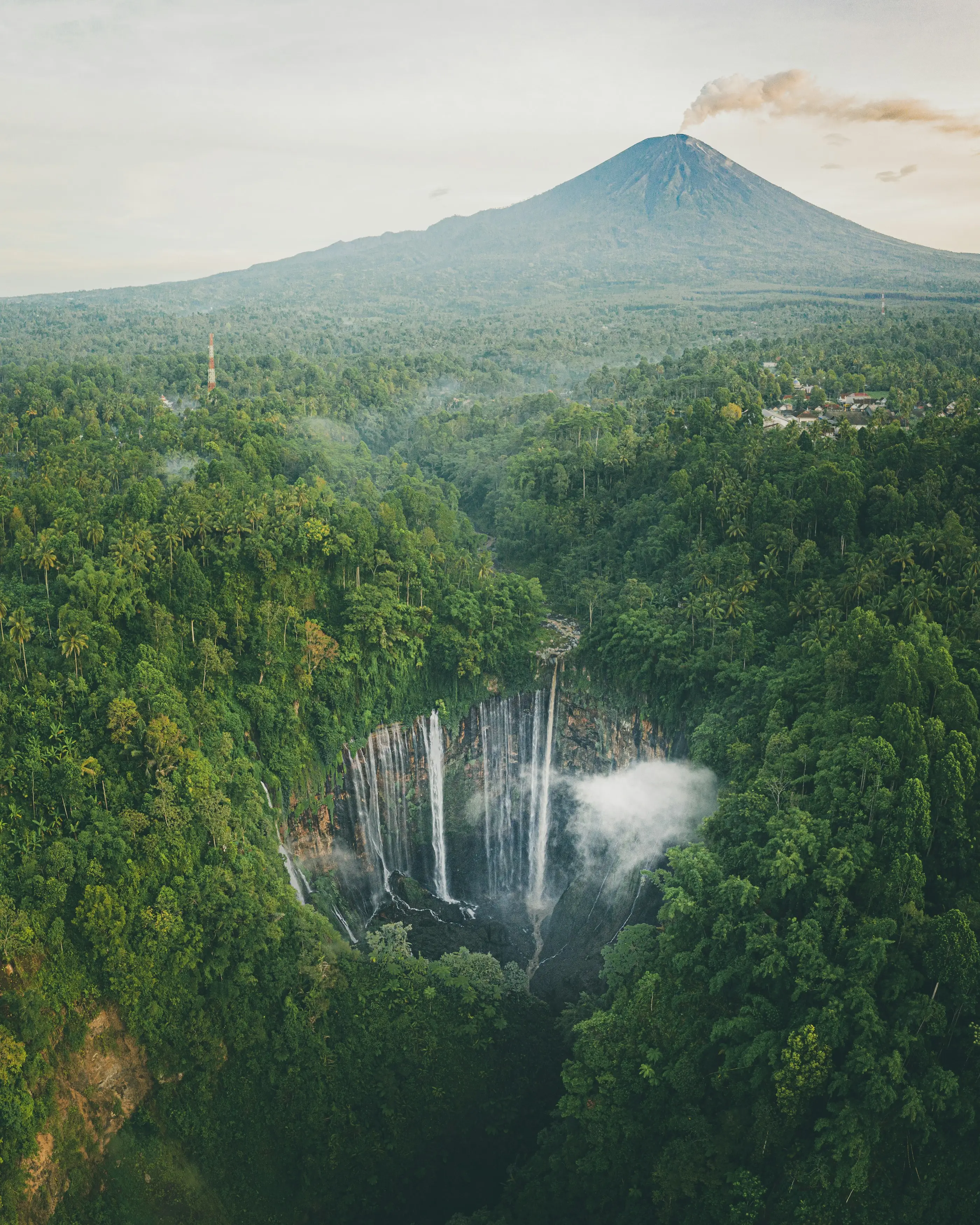 Smoking tropical volcano above a jungle-covered valley with a waterfall gorge